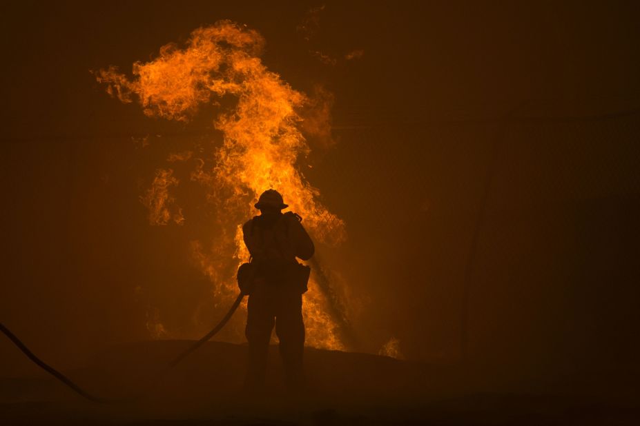 A firefighter hoses down burning pipes near a water tank.