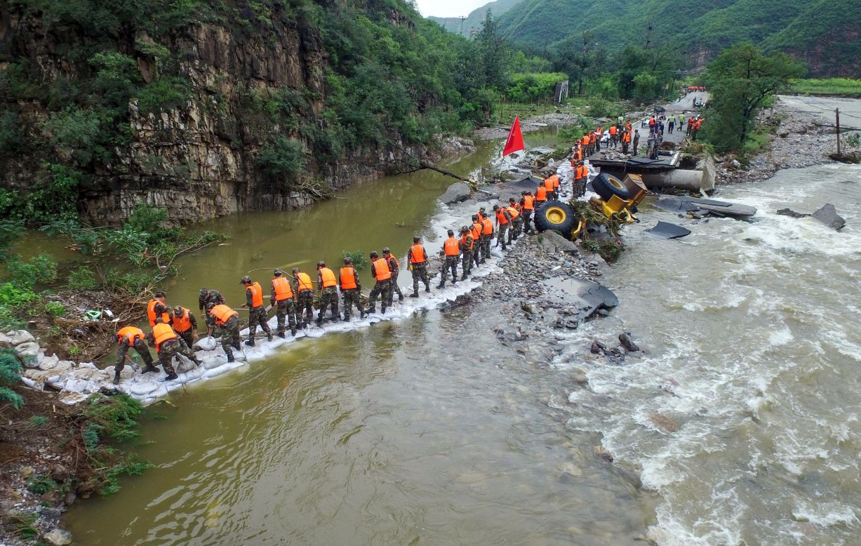 This photo taken on July 21 shows Chinese soldiers carrying sandbags to reinforce a damaged road hit by heavy rainstorms in Fangshan District in Beijing.