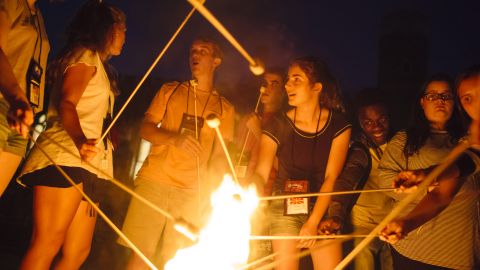 Campers at the retreat roast marshmallows over a fire together.