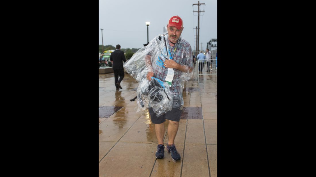 A cameraman carries gear through a rainstorm outside the arena.