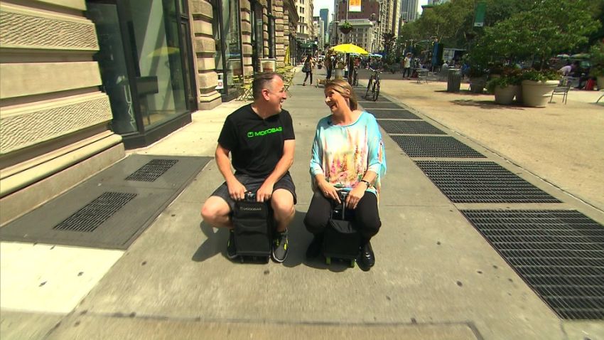 Now you can ride your suitcase. CNN's Jeanne Moos took a test drive on a motorized suitcase.      Why carry your luggage when it can carry you? Now you can ride your suitcase along those long airport hallways. Video of Modobag has gone viral and today I got to test drive a suitcase on NYC sidewalks. The bag is designed to fit as carryon. It has handlebars that pop up and foot holds that pop out. Very James Bond to convert it from luggage to a suitcase you can ride on. Top speed is 8 miles an hour and it handles well. The creator and I drove alongside one another discussing intricacies like ?how come no turn signals?? At least I didn?t mow anyone down driving my suitcase.
