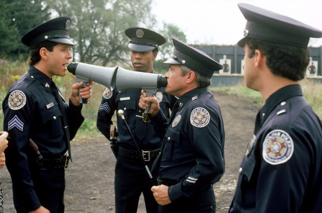 Steve Guttenberg as Mahoney and G.W. Bailey as Captain Harris in conversation while Michael Winslow looks on in a scene from a "Police Academy" film.  