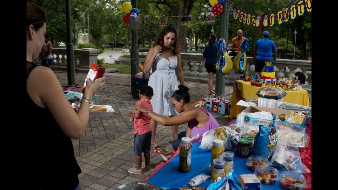 A woman sprays insect repellant on her child at a birthday party in a San Juan park.
