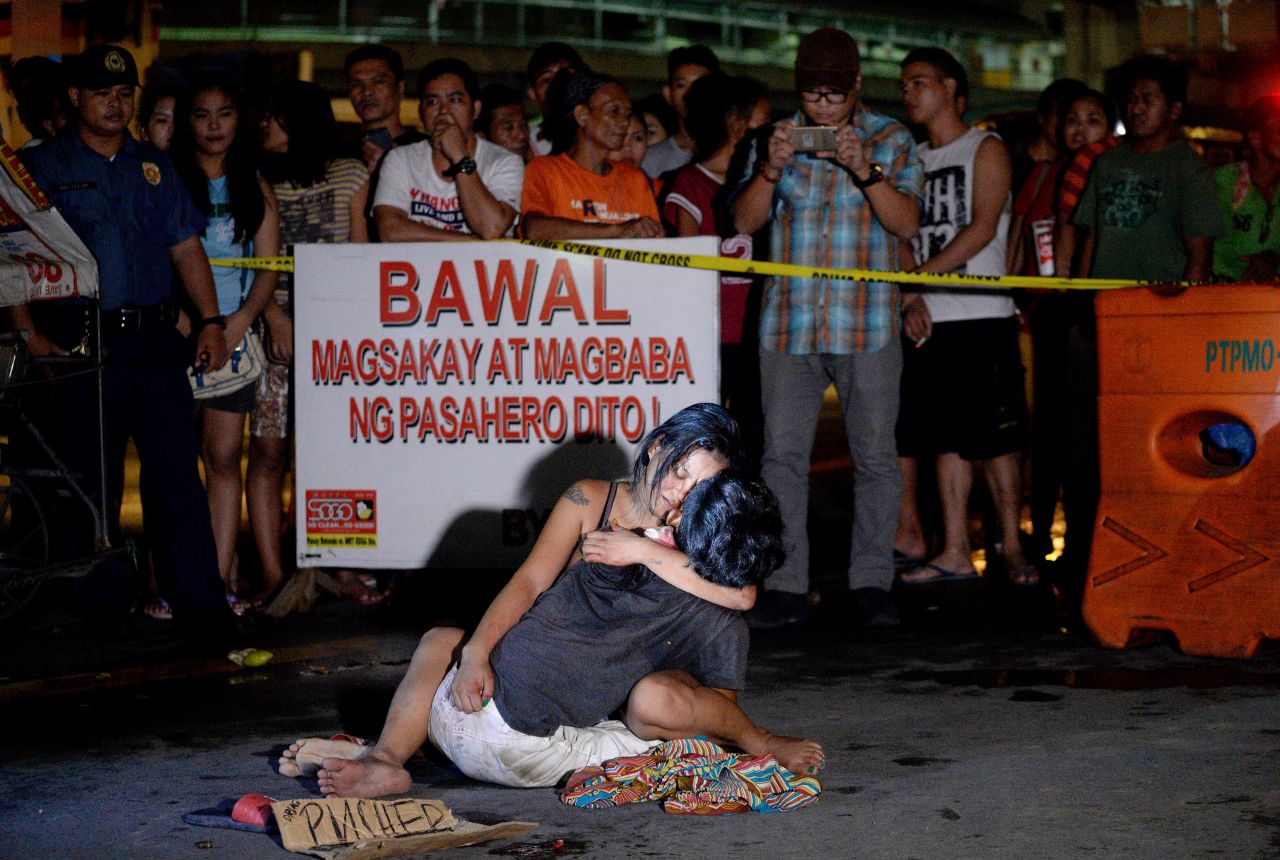 A woman cradles her husband, next to a placard which reads "I'm a pusher," who was shot dead in Manila on July 23, 2016. 
