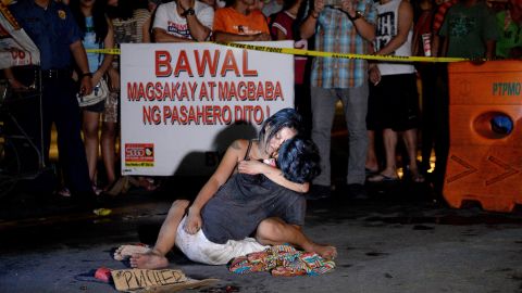 Jennilyn Olayres hugs her partner, Michael Siaron, on the street where he was shot. Next to him is a placard which reads "I'm a pusher."