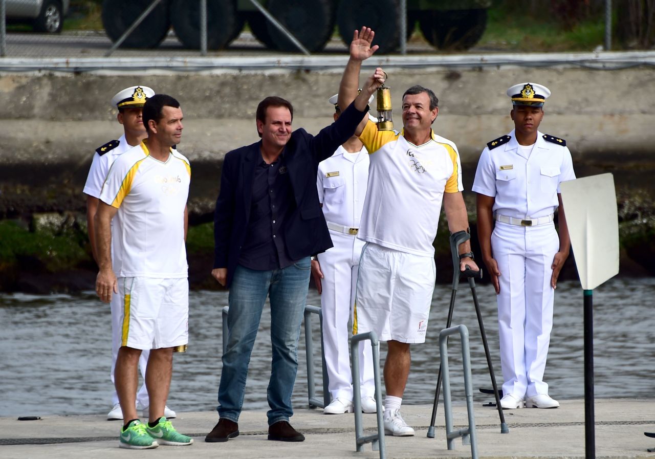 Paes (center) receives the Olympic Torch from Brazilian Olympians Torben Grael and his brother Lars.