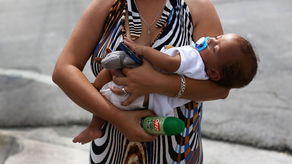 Barbara Betancourt holds her baby Daniel Valdes after being given a can of insect repellent by Miami Police officer James Bernat.