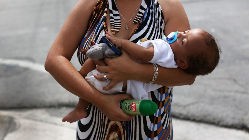 Barbara Betancourt holds her baby Daniel Valdes after being given a can of insect repellent by James Bernat, a City of Miami police officer, as he helps people living around the Miami Rescue Mission prevent mosquito bites that may infect them with the Zika virus on August 2, 2016 in Miami, Florida. A reported 14 individuals have been infected with the Zika virus by local mosquitoes.
