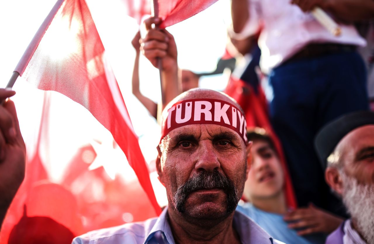 A man wears a headband reading "Turkey" as thousands wave Turkish flags around him.