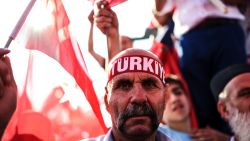 A man wears a headband reading "Turkey" as thousands wave Turkish flags around him.