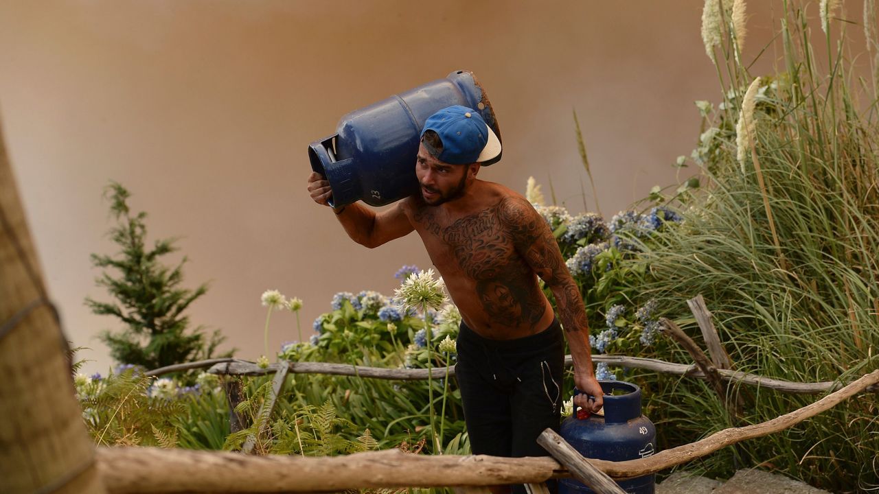 A man carries gas cylinders as a wildfire blazes in Funchal, Madeira.
