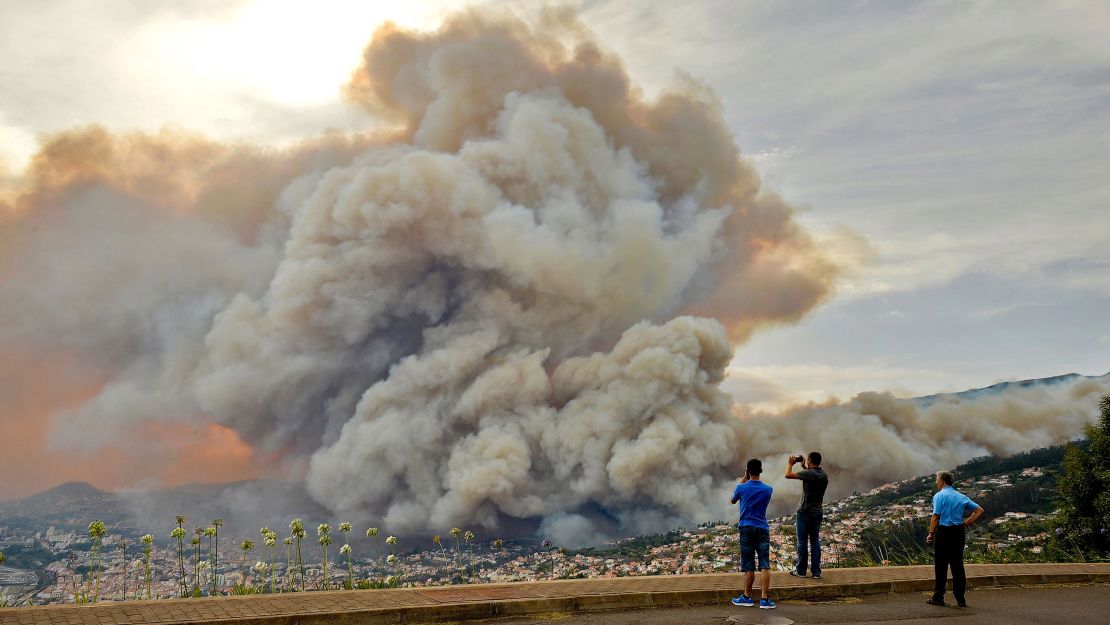 Bystanders photograph the smoke cloud rising from a wildfire on Madeira.