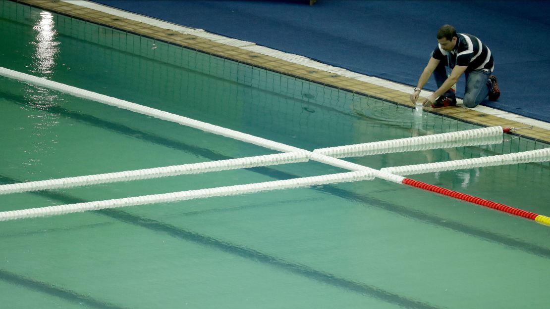 An inspector takes a sample from the water polo pool which turned green in color.