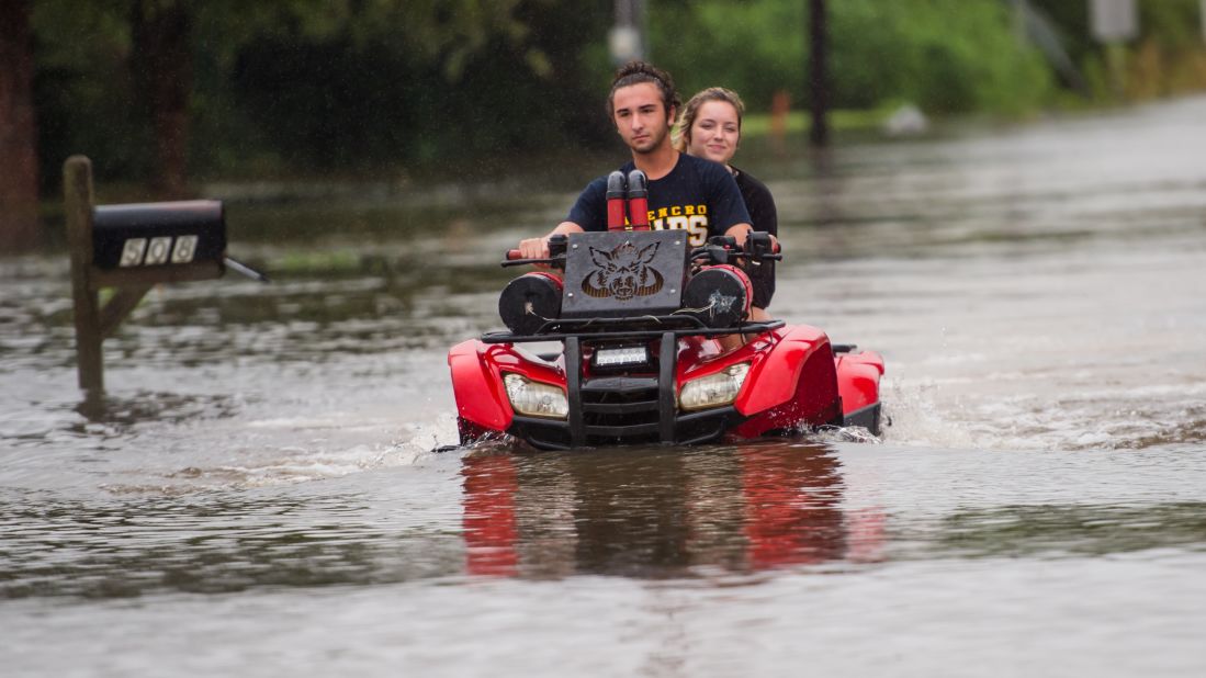 People ride an all-terrain vehicle through a flooded neighborhood in Carencro, Louisiana, on August 13.