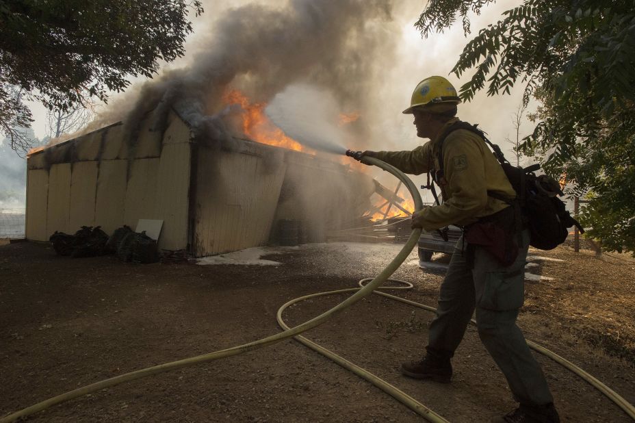 Tyrol Martin of the US Forest Service douses flames as a structure burns near the town of Lower Lake, California on Sunday, August 14. Flames continue to burn out of control in the area. A wildfire destroyed at least four homes and forced thousands of people in two Northern California towns to flee on Sunday as flames jumped a road and moved into populated areas. 