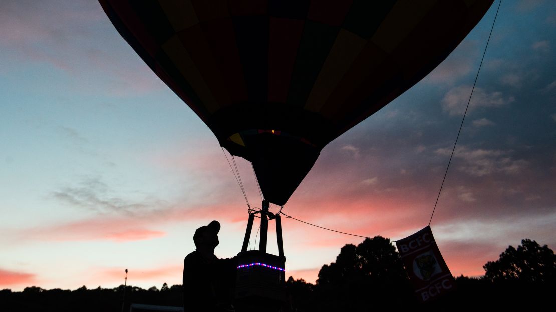 A model hot air balloon is held just above the ground as the sun goes down over Ashton Court.