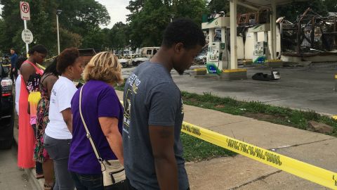 A ground of people pray in front of a burned gas station in Sherman Park.