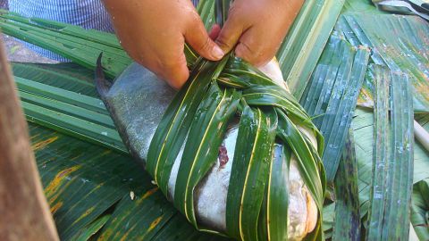 A fish is wrapped in taro leaves ahead of being cooked. 