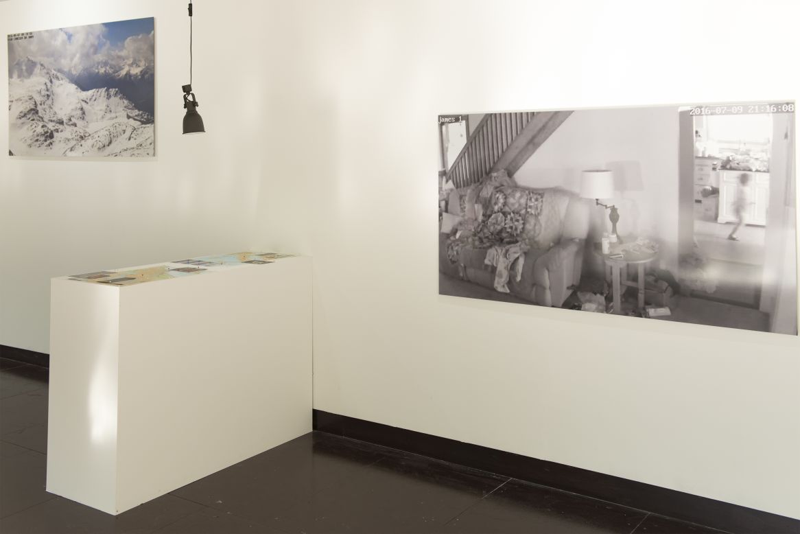 The exhibition is held at Cass School of Art & Architecture's Bank Gallery in London. On the wall is a photo of a house where the blurry figure of small child running can be seen. 