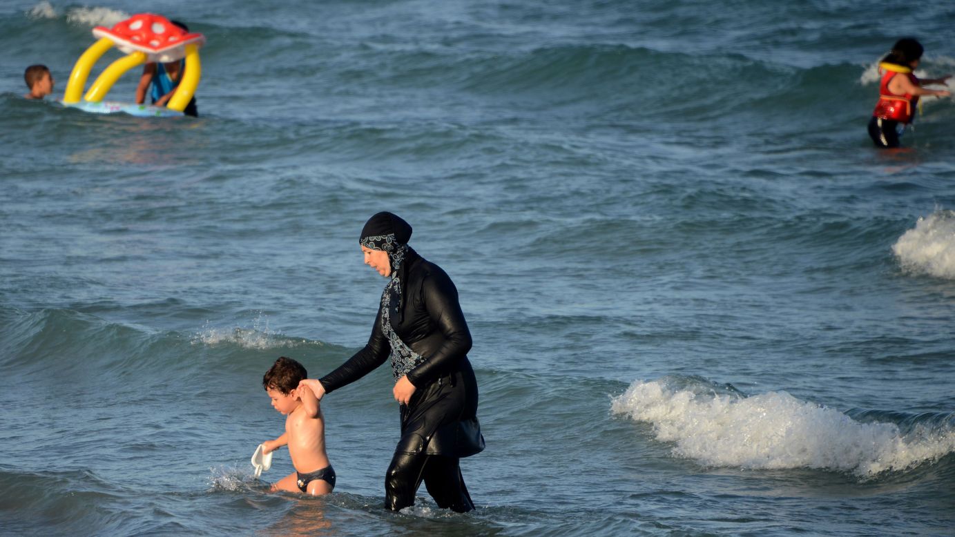 <strong>Burkini:</strong> The full-body swimsuit worn by Muslim women leaves only the face, hands and feet exposed. Here a woman in a burkini wades in the water with a child at Ghar El Melh beach in Tunisia.