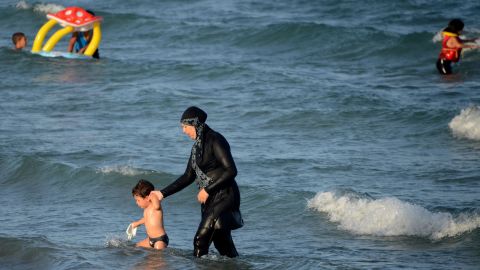 <strong>Burkini:</strong> The full-body swimsuit worn by Muslim women leaves only the face, hands and feet exposed. Here a woman in a burkini wades in the water with a child at Ghar El Melh beach in Tunisia.