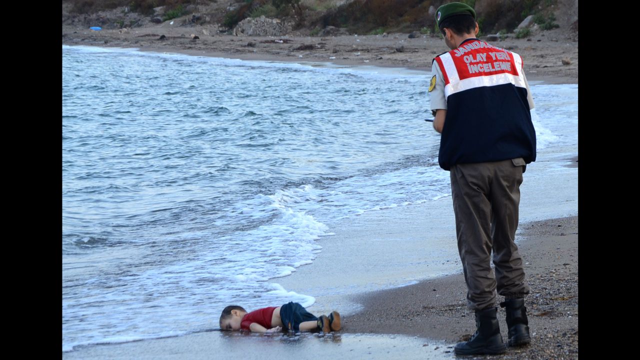A Turkish police officer stands next to a Alan Kurdi's body off the shores in Bodrum, Turkey, on September 2, 2015 after a boat carrying refugees sank while reaching the Greek island of Kos.