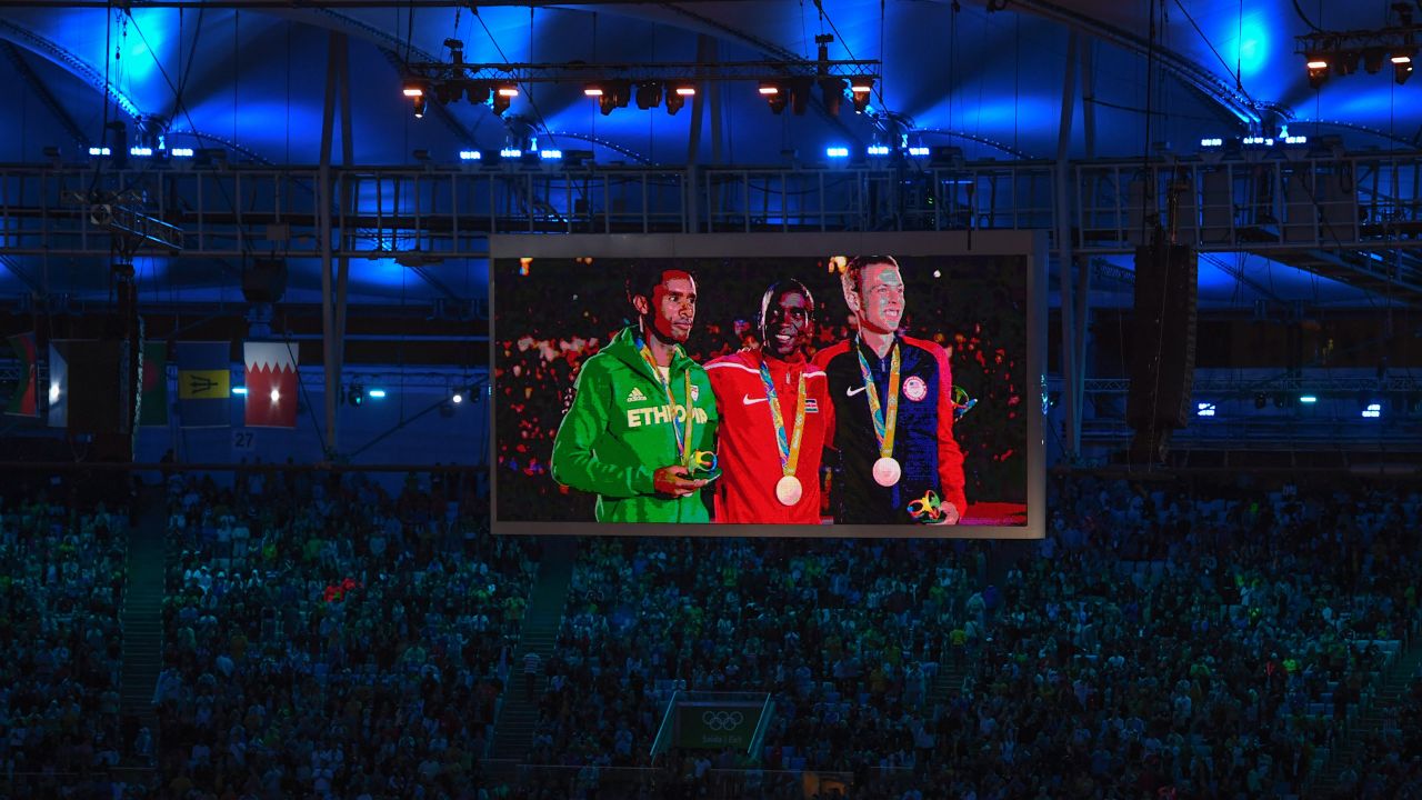 From left, men's marathon silver medalist Feyisa Lilesa of Ethiopia, gold medalist Eliud Kipchoge of Kenya and bronze medalist Galen Rupp of the United States are seen on a giant screen as they stand on the podium during the closing ceremony.