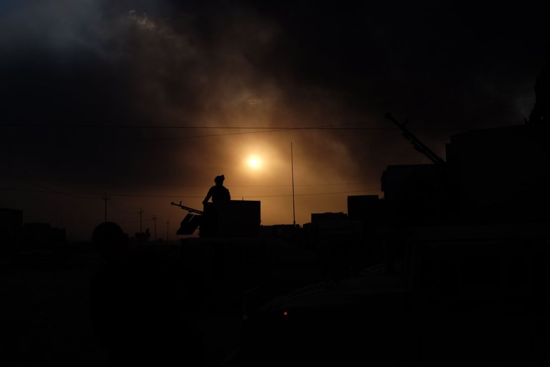 An Iraqi soldier stands guard on the outskirts of Qayyarah, under apocalyptic skies filled with smoke.