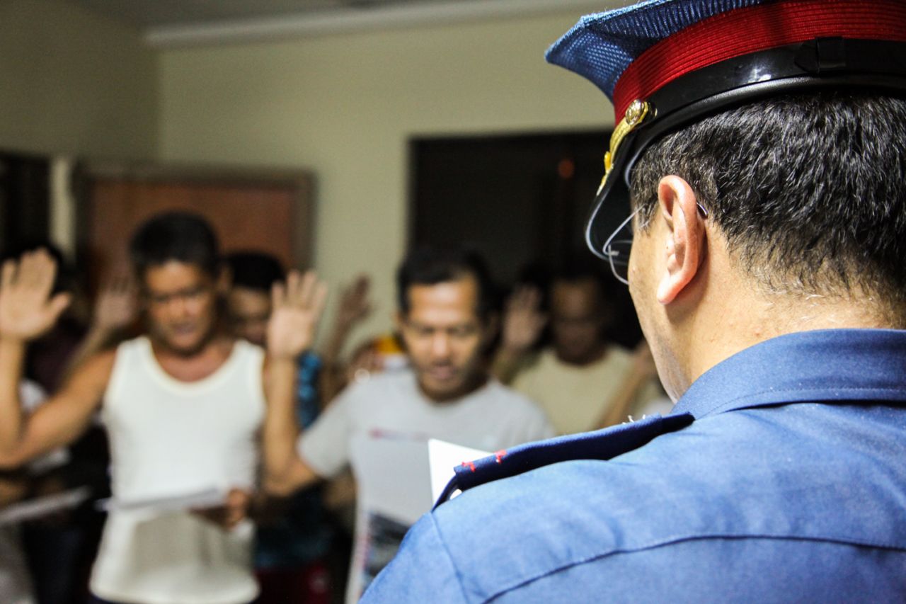 Hands raised, the detainees recite a pledge that affirms that their surrender is voluntary. They promise to "undertake to stop all" drug-related activities.