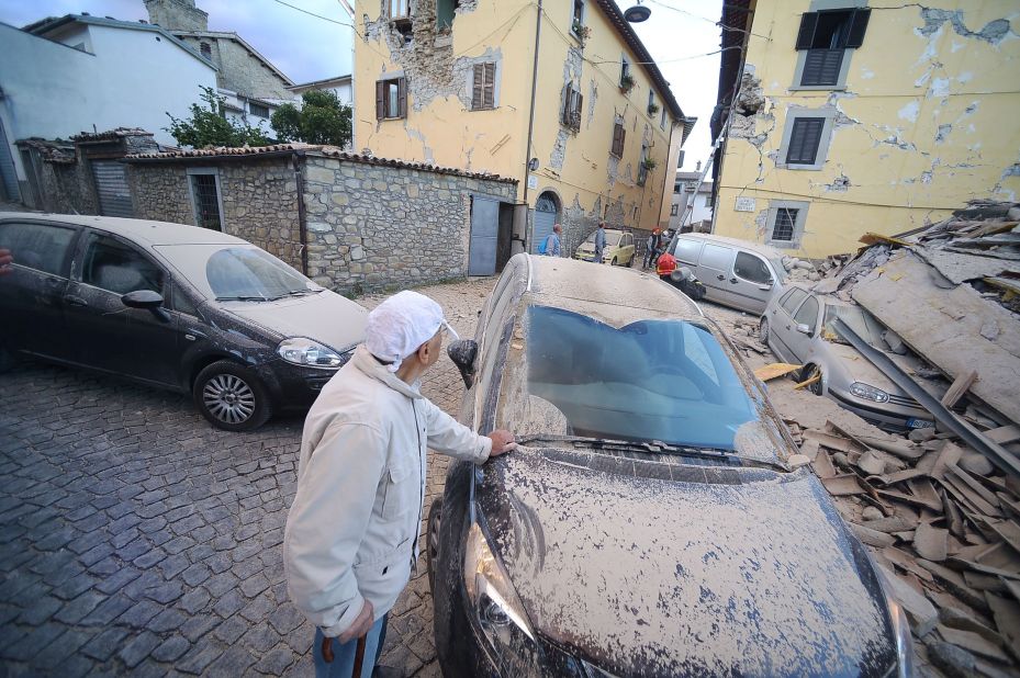 A man surveys damage near a dust-covered car in Amatrice on August 24.