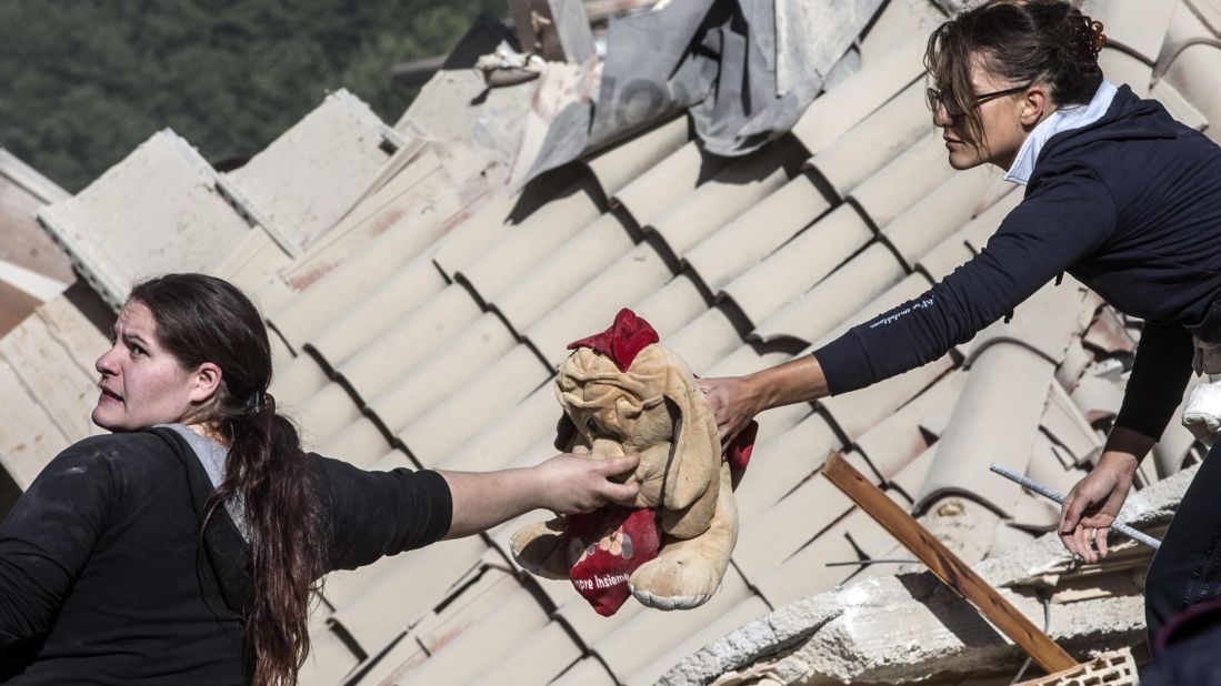 Two women pass along a stuffed toy in Amatrice on August 24.