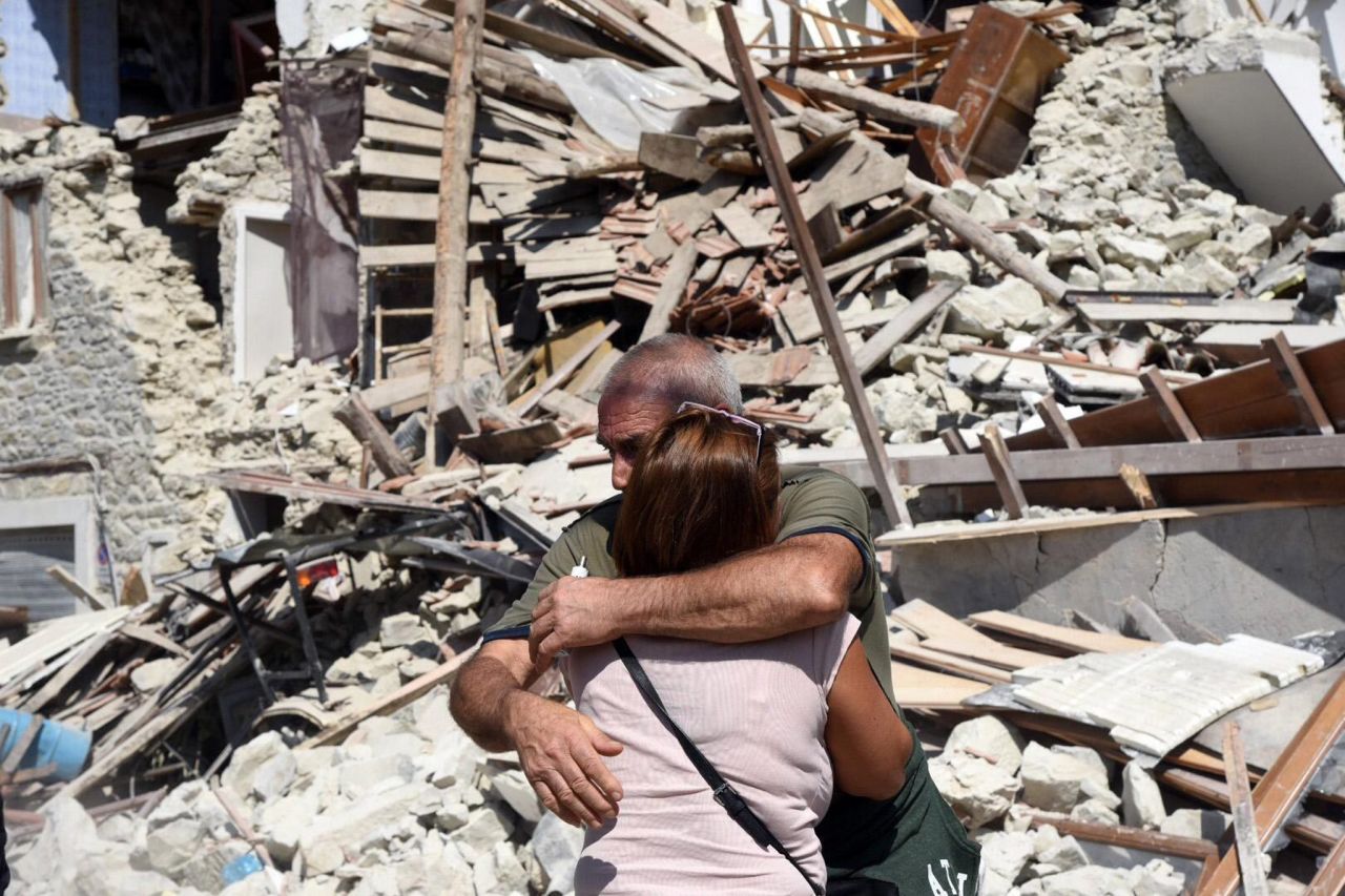 Two people hug each other next to damaged houses in Pescara del Tronto.