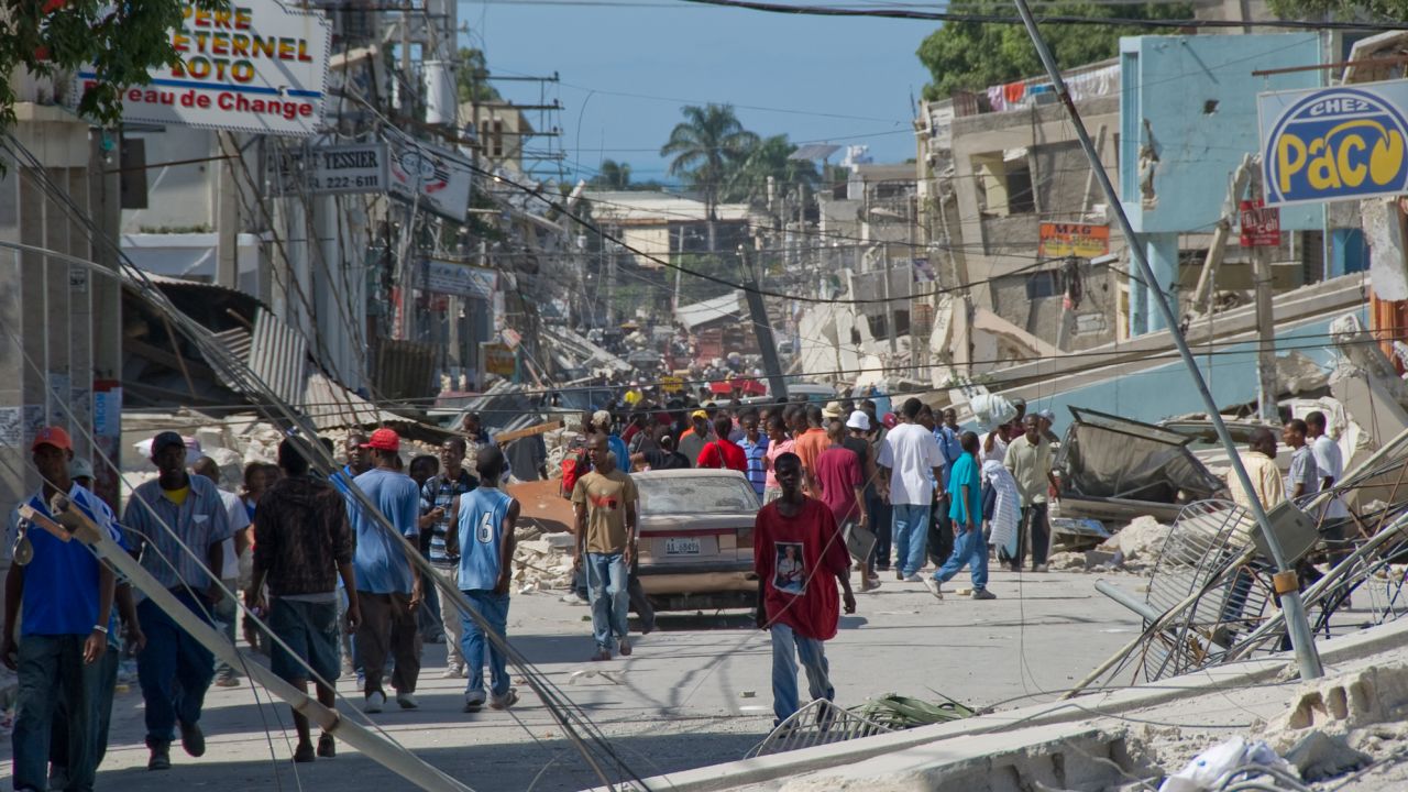 People wander the streets in front of the remains of a boarding school in the downtown area January 13, 2010 in Port-au-Prince, Haiti.
