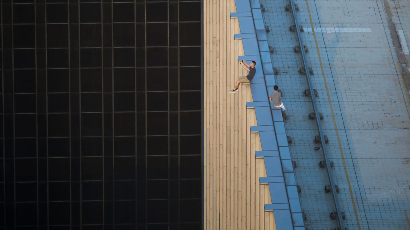 People take photos as they sit on the ledge of a high-rise building in Hong Kong on Tuesday, August 23.
