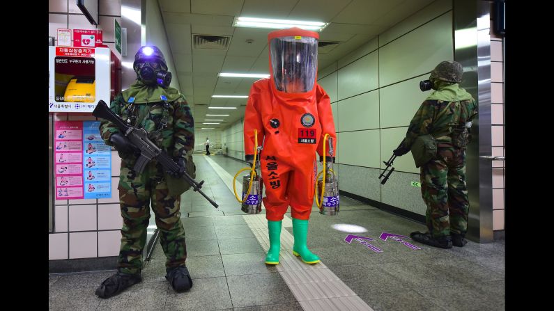 A person wearing full protective gear, center, stands with soldiers wearing gas masks during a joint South Korea-US anti-terror drill at a subway station in Seoul, South Korea, on Tuesday, August 23.