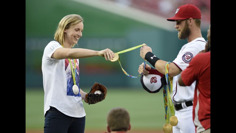 US swimmer Katie Ledecky, left, hands her medals to Bryce Harper of the Washington Nationals baseball team on Wednesday, August 24. Ledecky, who won four gold medals and one silver at the Summer Olympics, threw the ceremonial first pitch.