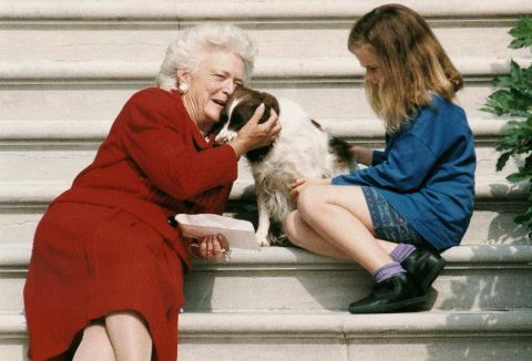 First lady Barbara Bush talks to her dog, Millie, as she and granddaughter Barbara Bush wait for President George H.W. Bush to return to the White House on September 13, 1991.