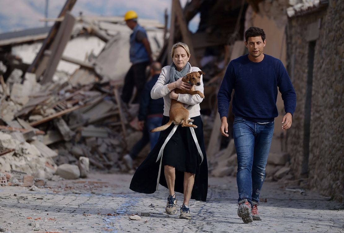 A woman holds a dog as she and a man hurry past rubble in Amatrice.