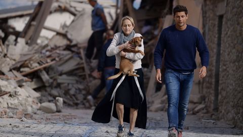 A woman holds a dog as she and a man hurry past rubble in Amatrice.