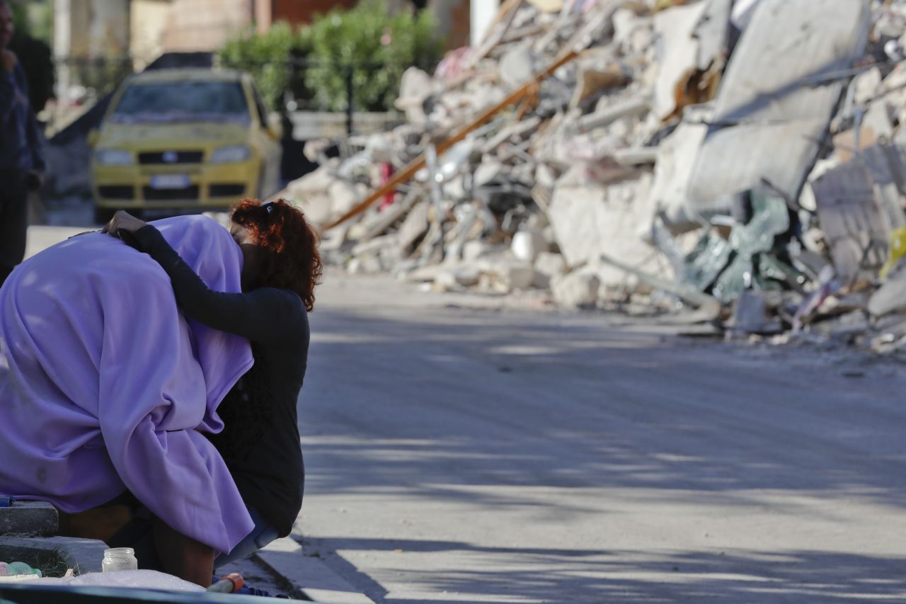 A man and woman comfort each other in front of a collapsed house in Amatrice on August 26.