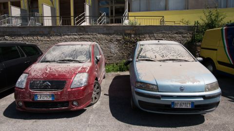 Cars caked in a layer of thick debris dust are parked in central Amatrice.