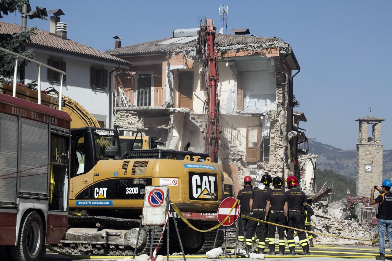 Firefighters stand by an excavator in Amatrice, Italy,on August 28, as dangerously damaged buildings and overhanging ledges are pulled down.  