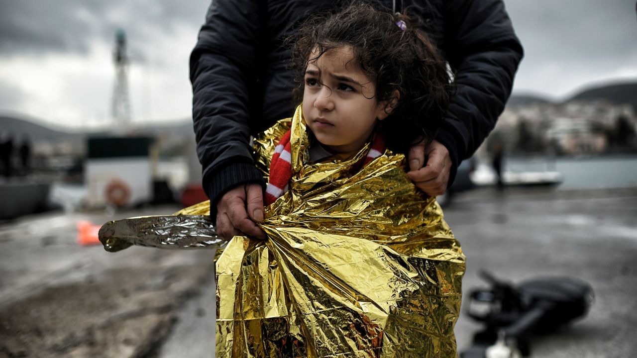 A father stands with his daughter as refugees and migrants arrive on the Greek island of Lesbos after crossing the Aegean Sea.
