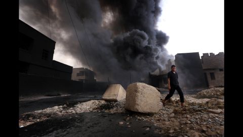 An Iraqi man walks near smoke billowing from oil wells, set ablaze by ISIS before fleeing the oil-producing region of Qayyarah, on August 30, 2016. 