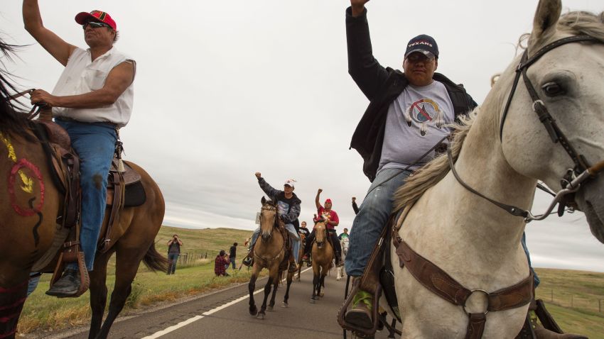 Native Americans ride with raised fists to a sacred burial ground that was disturbed by bulldozers building the Dakota Access Pipeline (DAPL), near the encampment where hundreds of people have gathered to join the Standing Rock Sioux Tribe's protest of the oil pipeline slated to cross the nearby Missouri River, September 4, 2016 near Cannon Ball, North Dakota.  
Protestors were attacked by dogs and sprayed with an eye and respiratory irritant yesterday when they arrived at the site to protest after learning of the bulldozing work. / AFP / ROBYN BECK        (Photo credit should read ROBYN BECK/AFP/Getty Images)