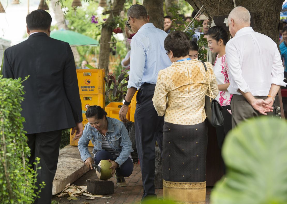 US President Barack Obama watches as a woman opens a coconut for him to drink as he makes a surprise stop for a drink alongside the Mekong River in Luang Prabang on September 7, 2016.