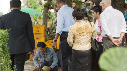 US President Barack Obama watches as a woman opens a coconut for him to drink as he makes a surprise stop for a drink alongside the Mekong River in Luang Prabang on September 7, 2016.