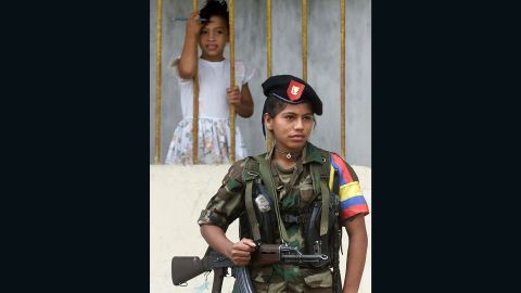 A young girl watches as a  FARC fighter stands guard in Los Pozos during peace talks in 2001.
