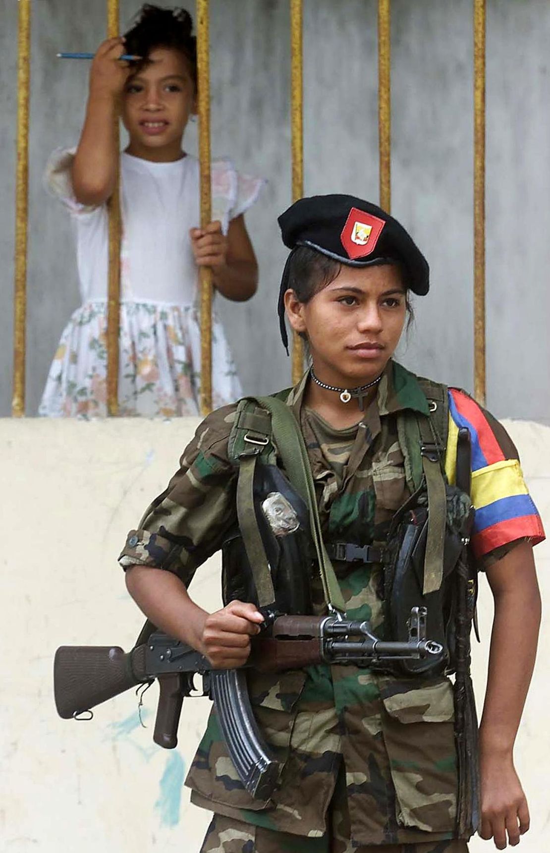 A young girl watches as a  FARC fighter stands guard in Los Pozos during peace talks in 2001.