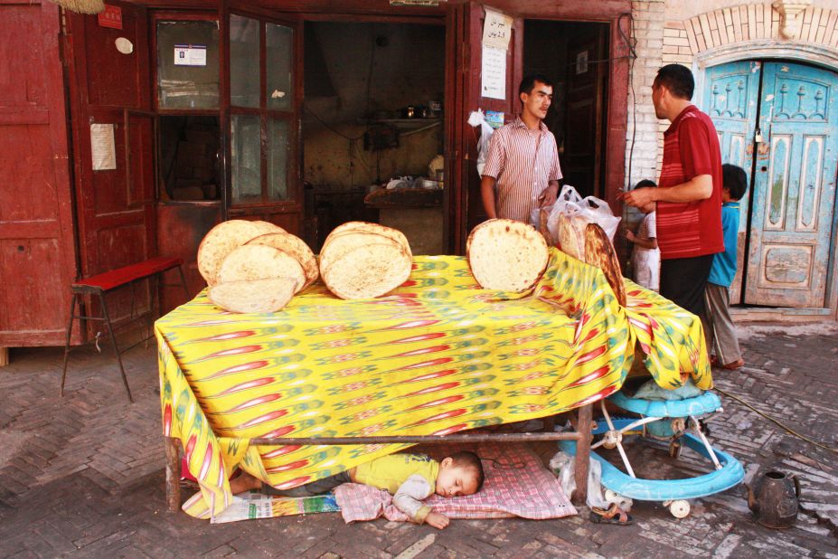 A young boy takes a nap beneath a stall selling Uyghur flatbread.